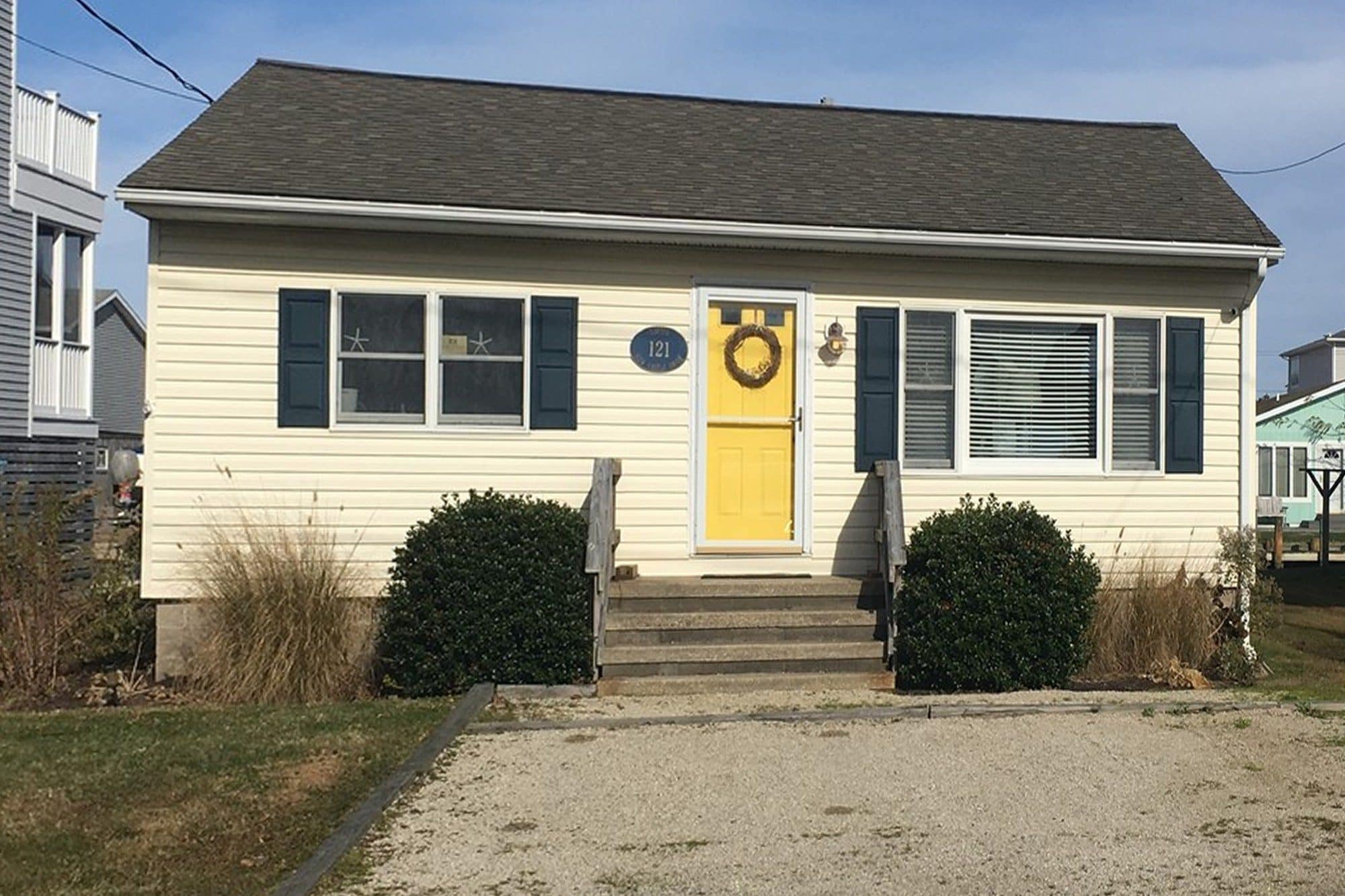 Before: a South Bethany cottage with yellow vinyl siding, navy shutters, and a yellow front door