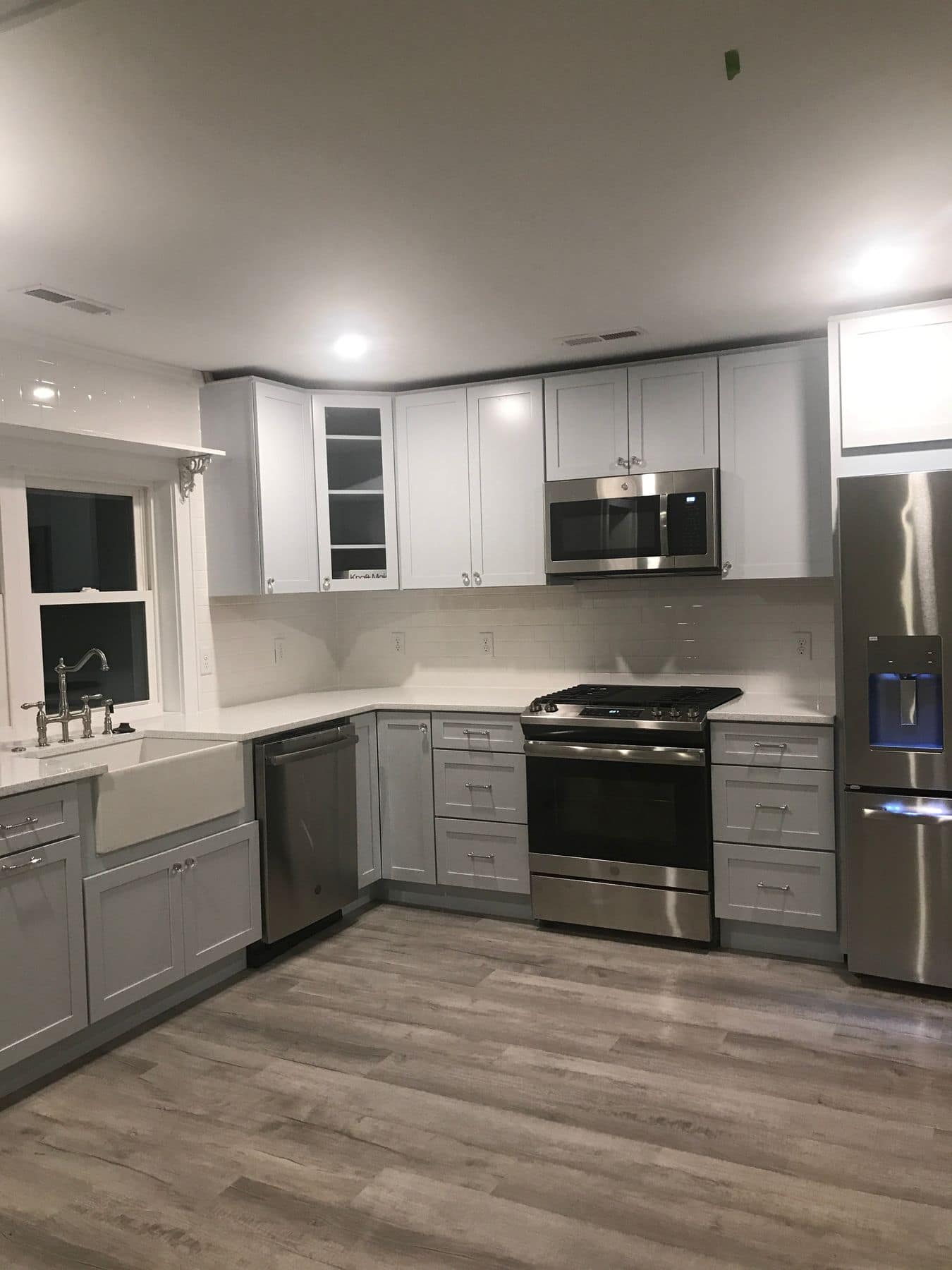 The new kitchen with white cabinets, stainless appliances, and a farmhouse sink under the window