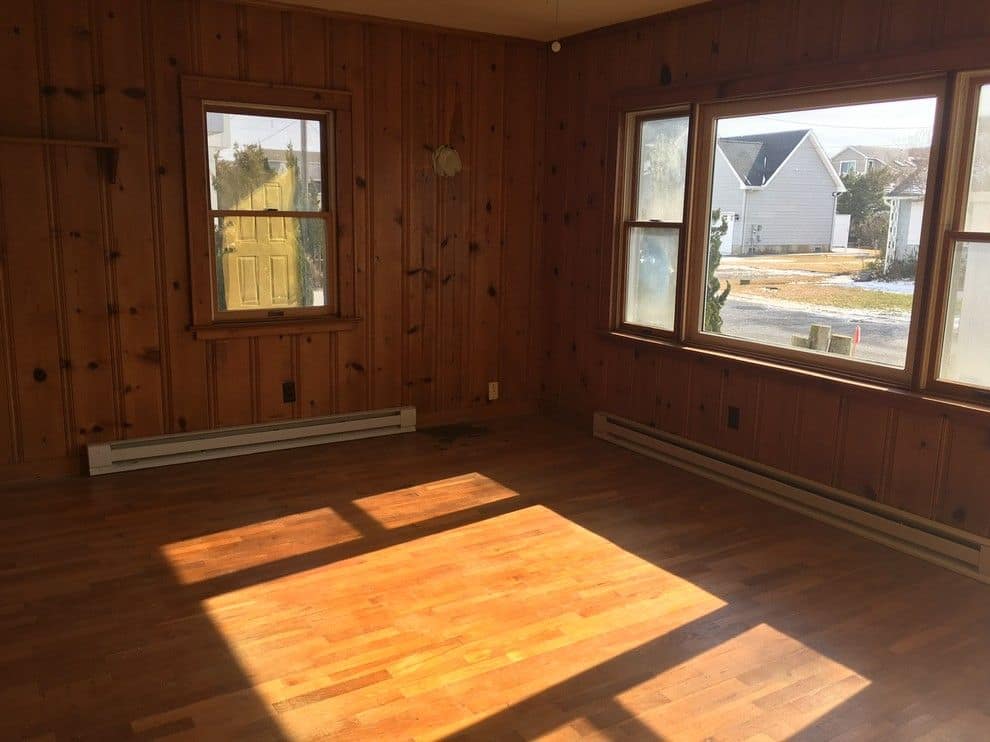 Before: the living room in dark knotty pine with an orange wood floor