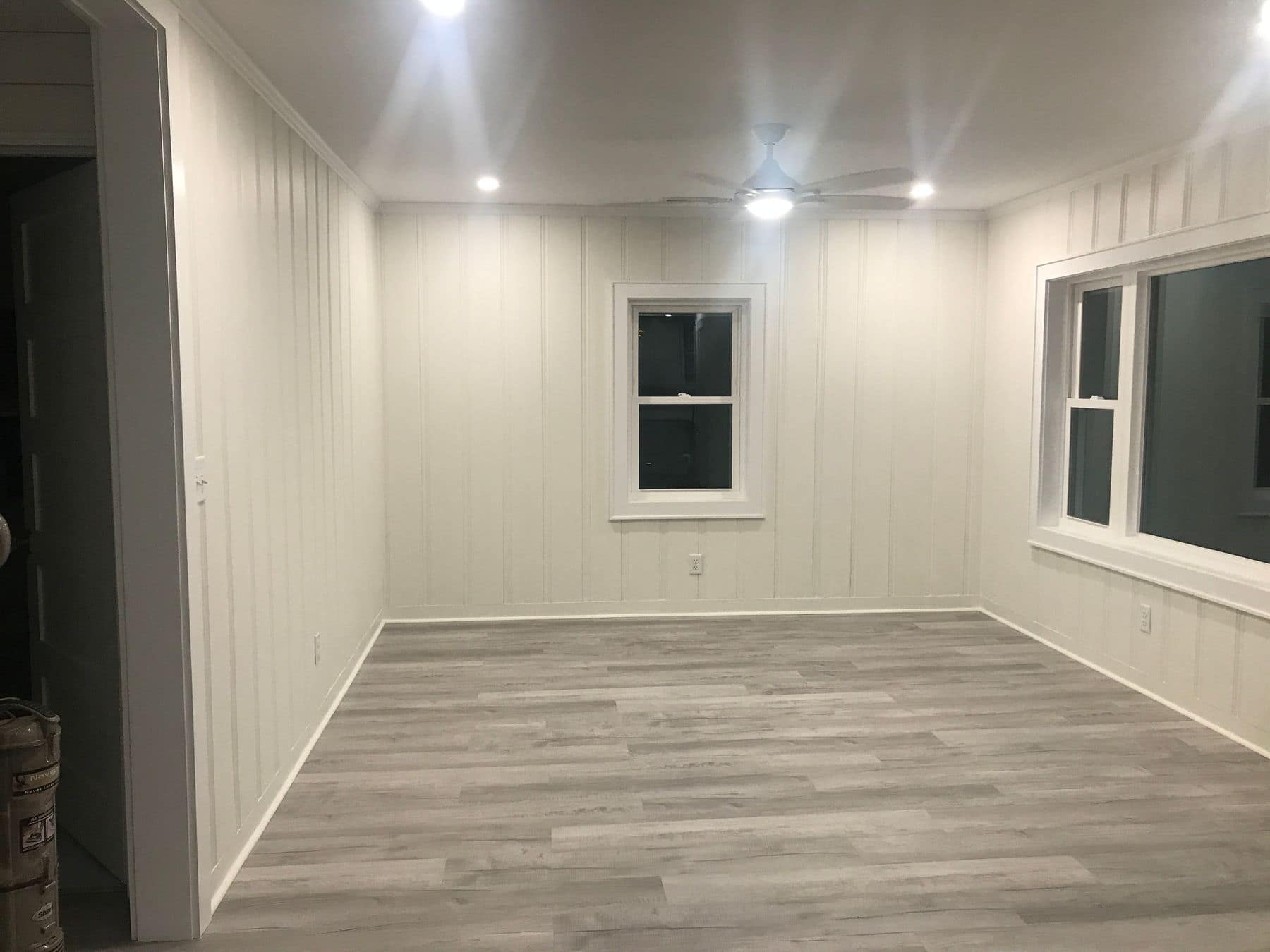 The living room with white vertical paneling, a gray plank floor, and recessed lights