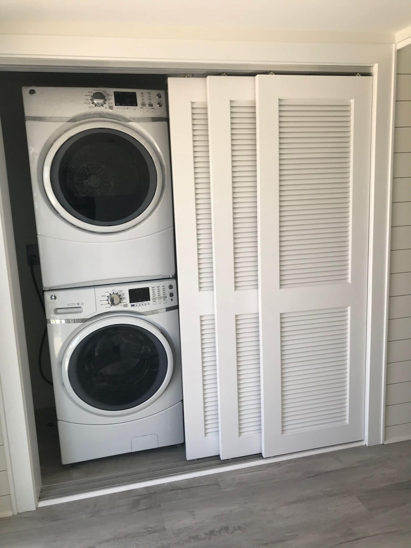 A stacked washer and dryer behind louvered doors