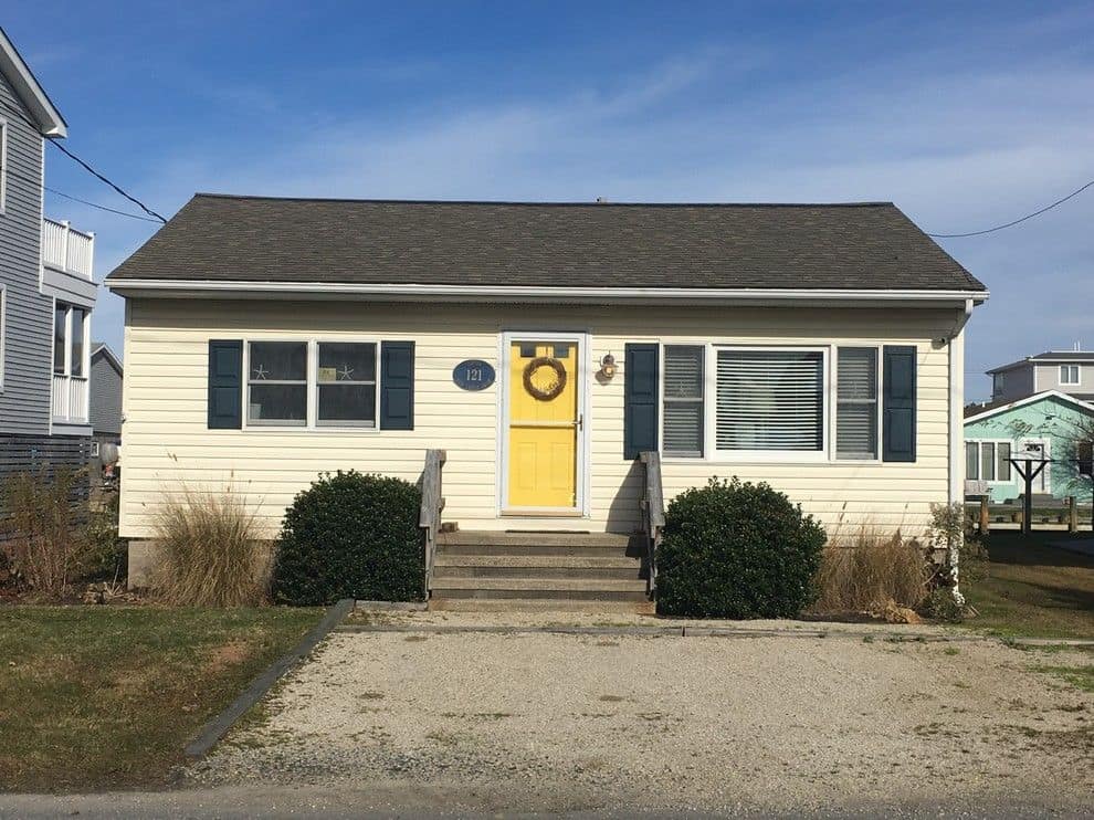 Before: the cottage with yellow siding, navy shutters, and a yellow front door